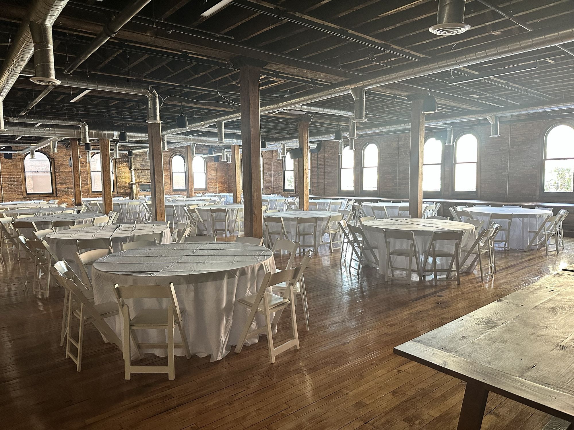 The Loft set for a dinner: round tables in white linen between timber posts, under arched brick windows